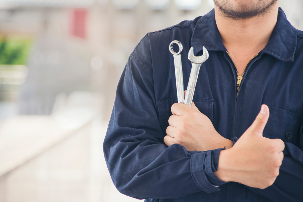 male mechanic giving thumbs up while holding 2 tools in other hand
