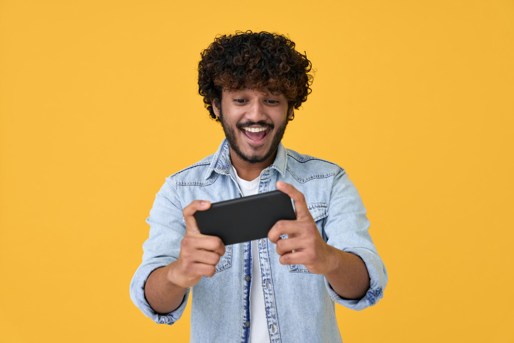 excited gamer playing using smartphone against yellow background